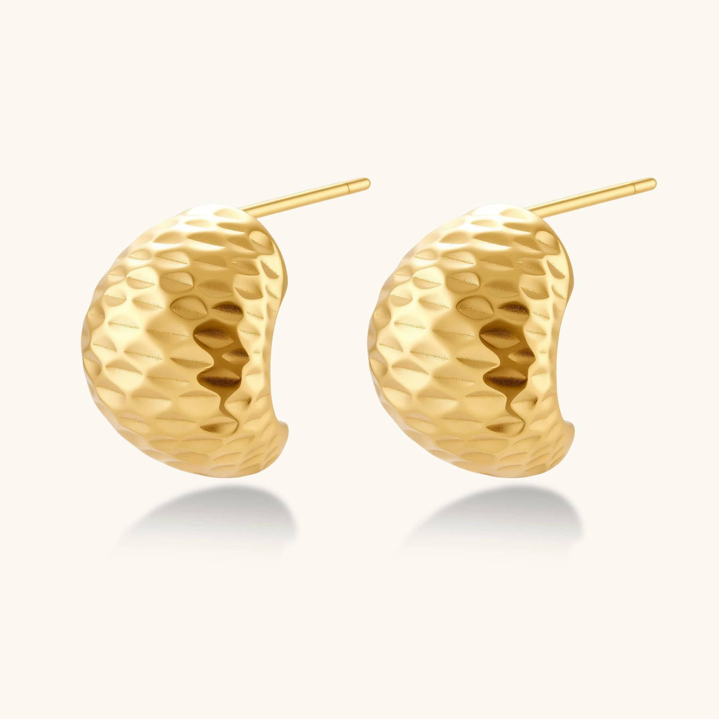 Pair of textured gold-plated sterling silver huggie earrings with dimpled surface finish on cream background.